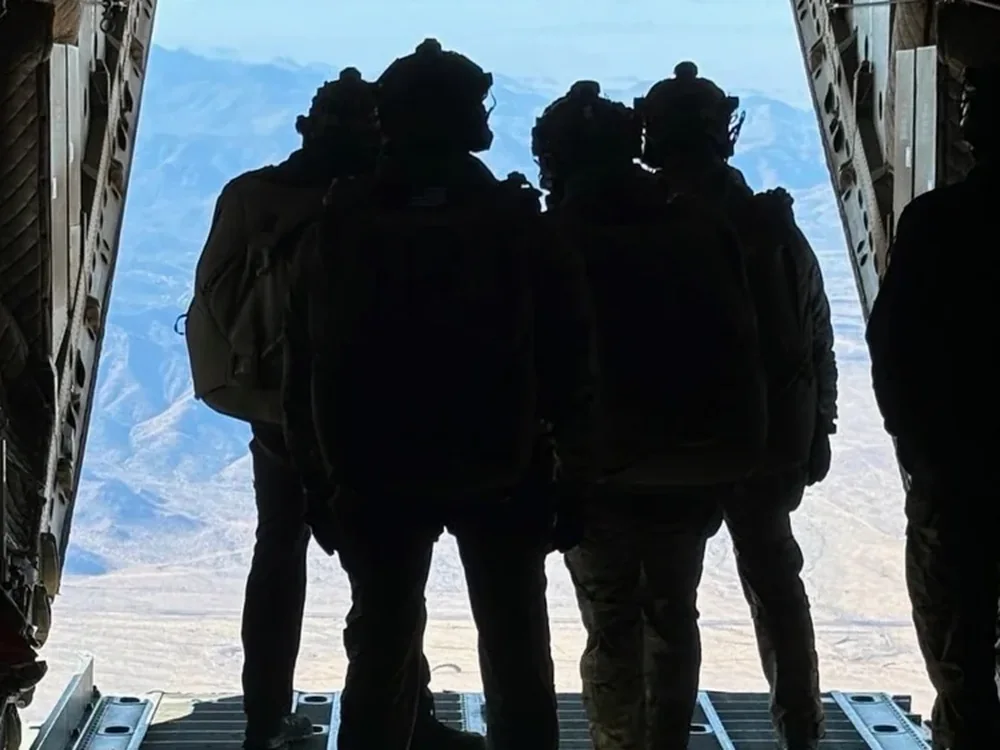 Four service members on the open ramp of an aircraft looking out over mountains